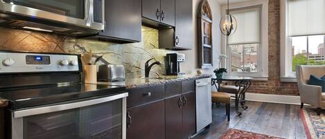 A modern kitchen with stainless steel appliances, dark cabinetry, and a large window providing a view of the city.