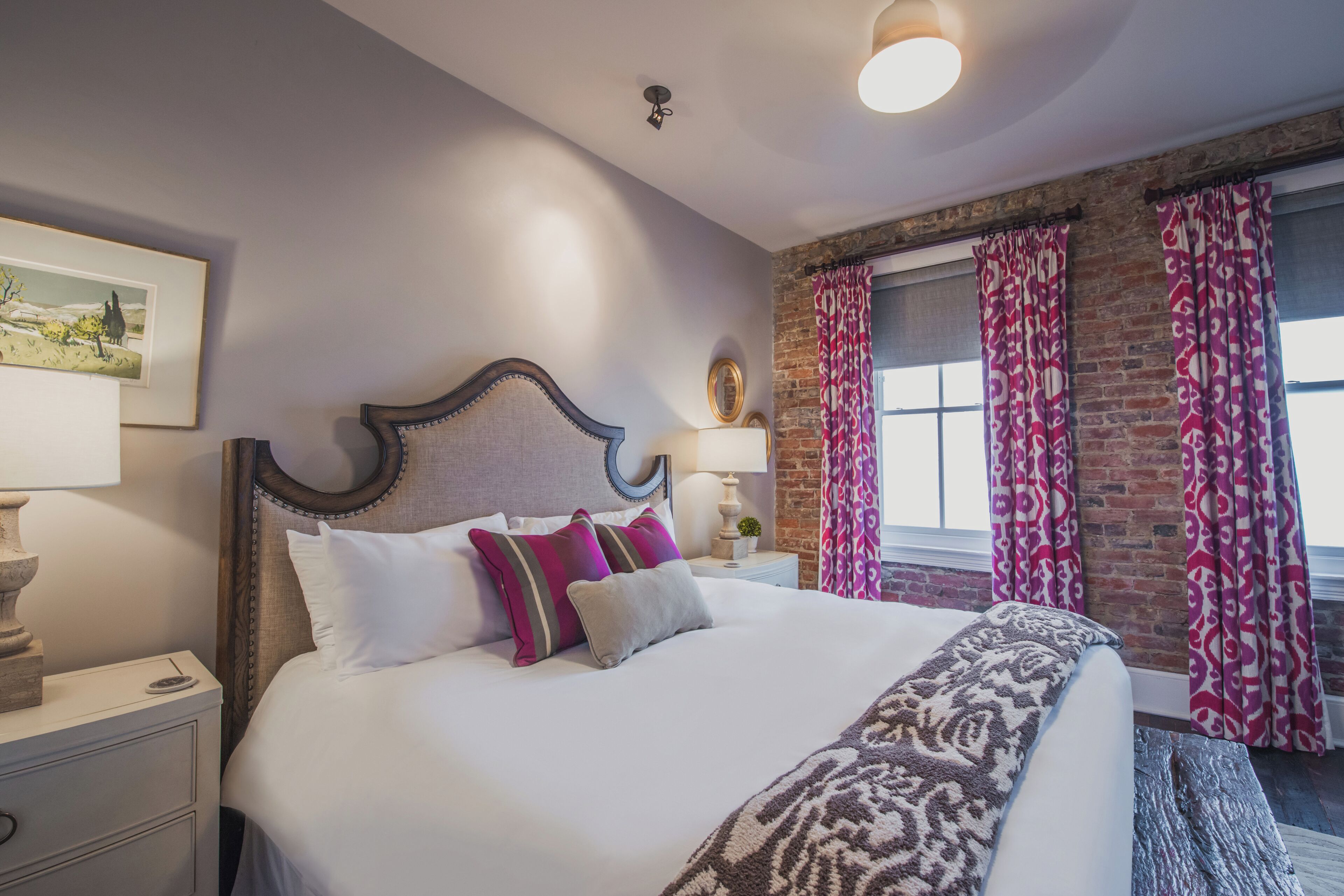 A neatly made bed with white and patterned bedding, a wooden headboard, and a nightstand with a lamp.