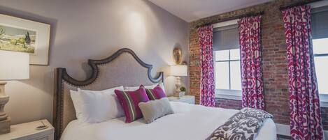 A neatly made bed with white and patterned bedding, a wooden headboard, and a nightstand with a lamp.