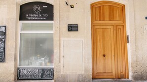 A building facade with a wooden door, a window with a sign reading "LA TABERNA DE TITO GASTRONOMIA ALICANTINA," and a sign indicating "COOKING IN PROGRESS."