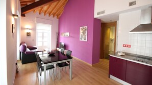 A modern kitchen with a purple accent wall, wooden ceiling beams, and a dining area with a table and chairs.
