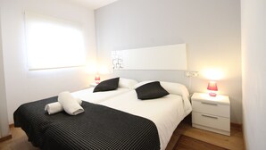A hotel room with two beds, a nightstand with a lamp, and a window with blinds.