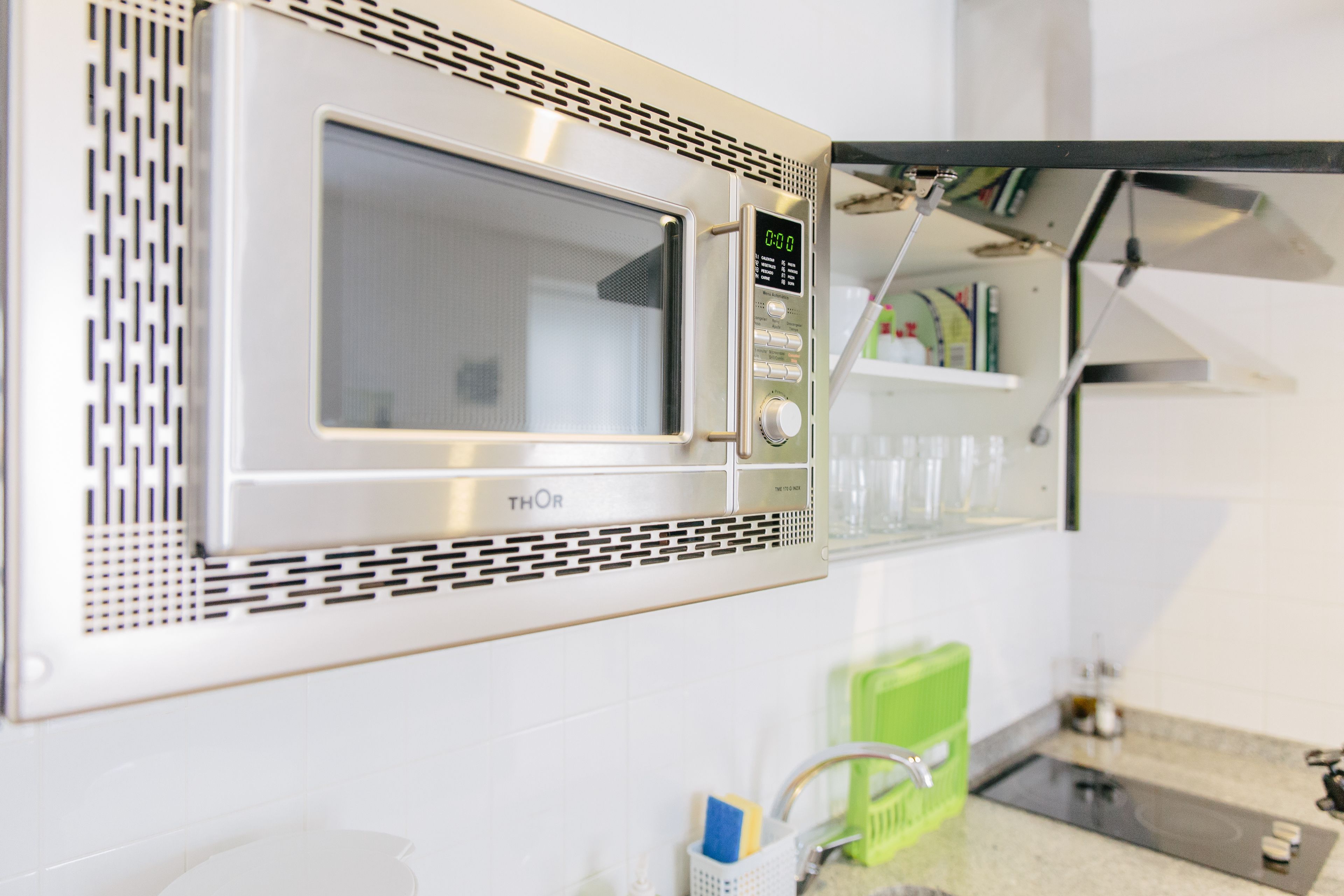 A kitchen with a built-in microwave, a sink, and a green dish rack.