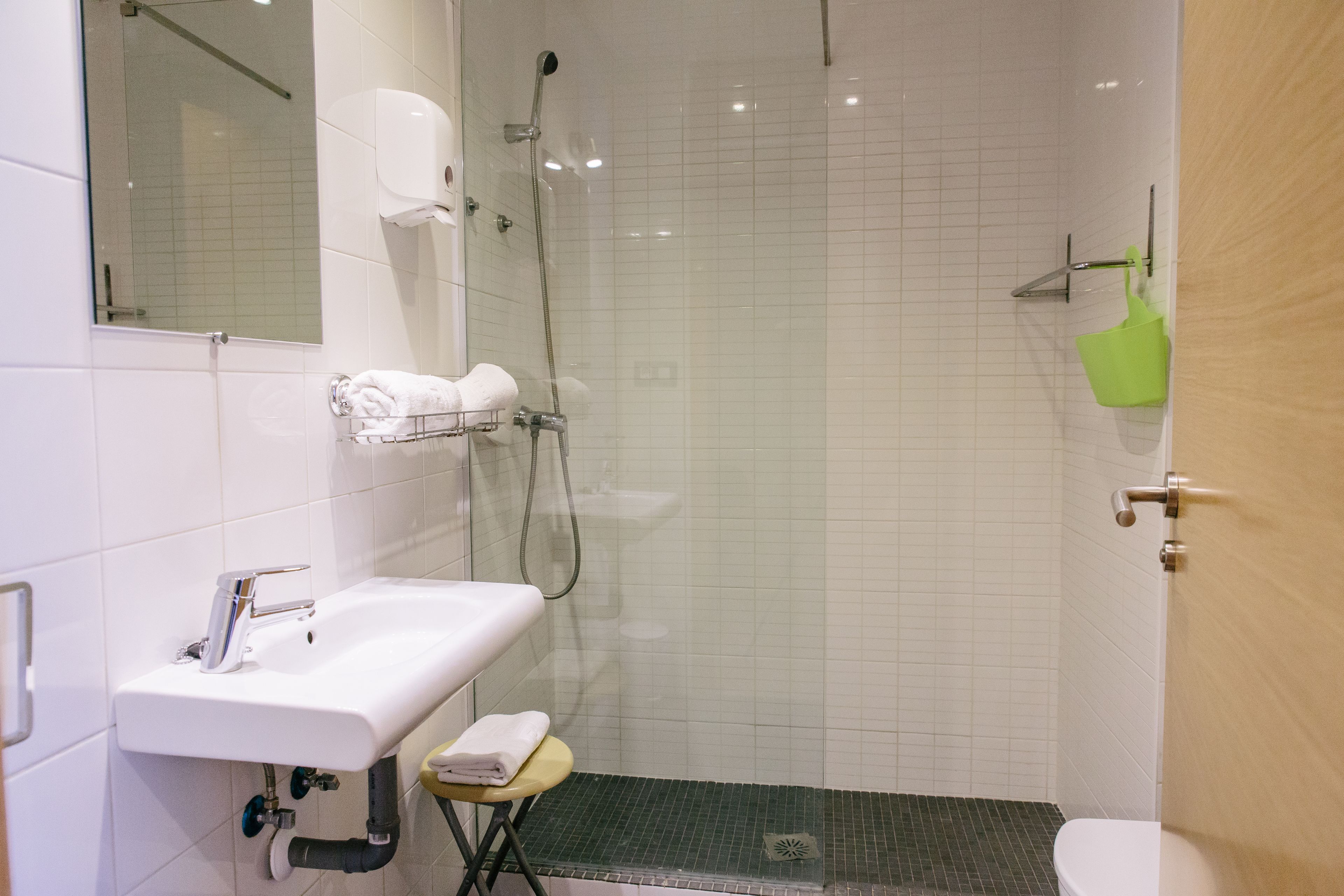 Ein Badezimmer mit einem weißen Waschbecken, einer Duschkabine aus Glas und einer grünen Badematte.