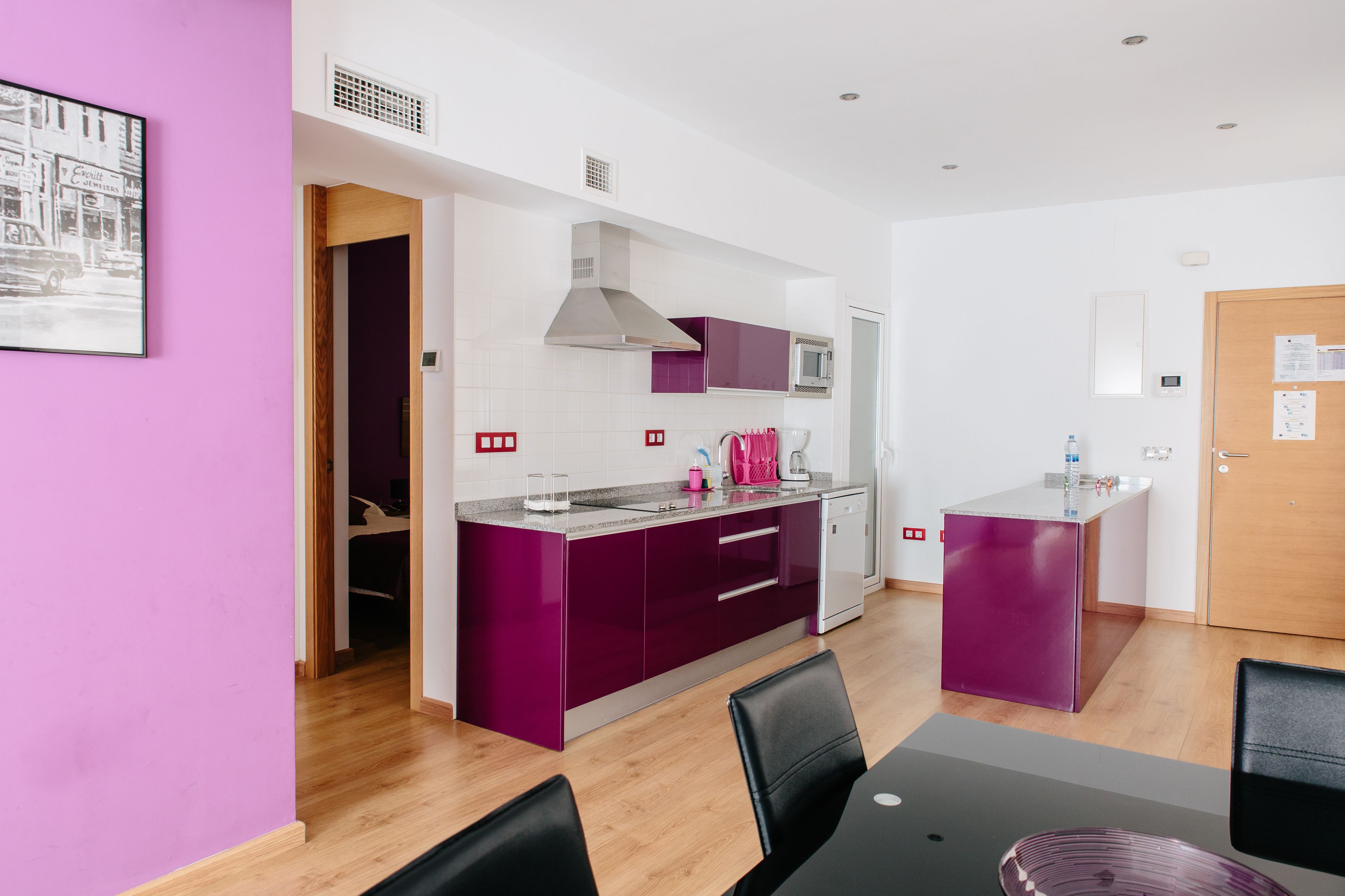 Una cocina moderna con armarios morados, un microondas y un lavamanos. Hay una zona de comedor con una mesa y sillas.