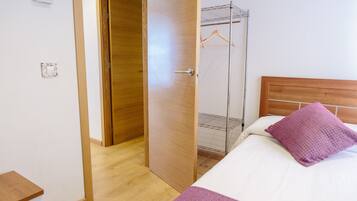 A bedroom with a wooden door, a metal rack, and a bed with a white and purple pillow.