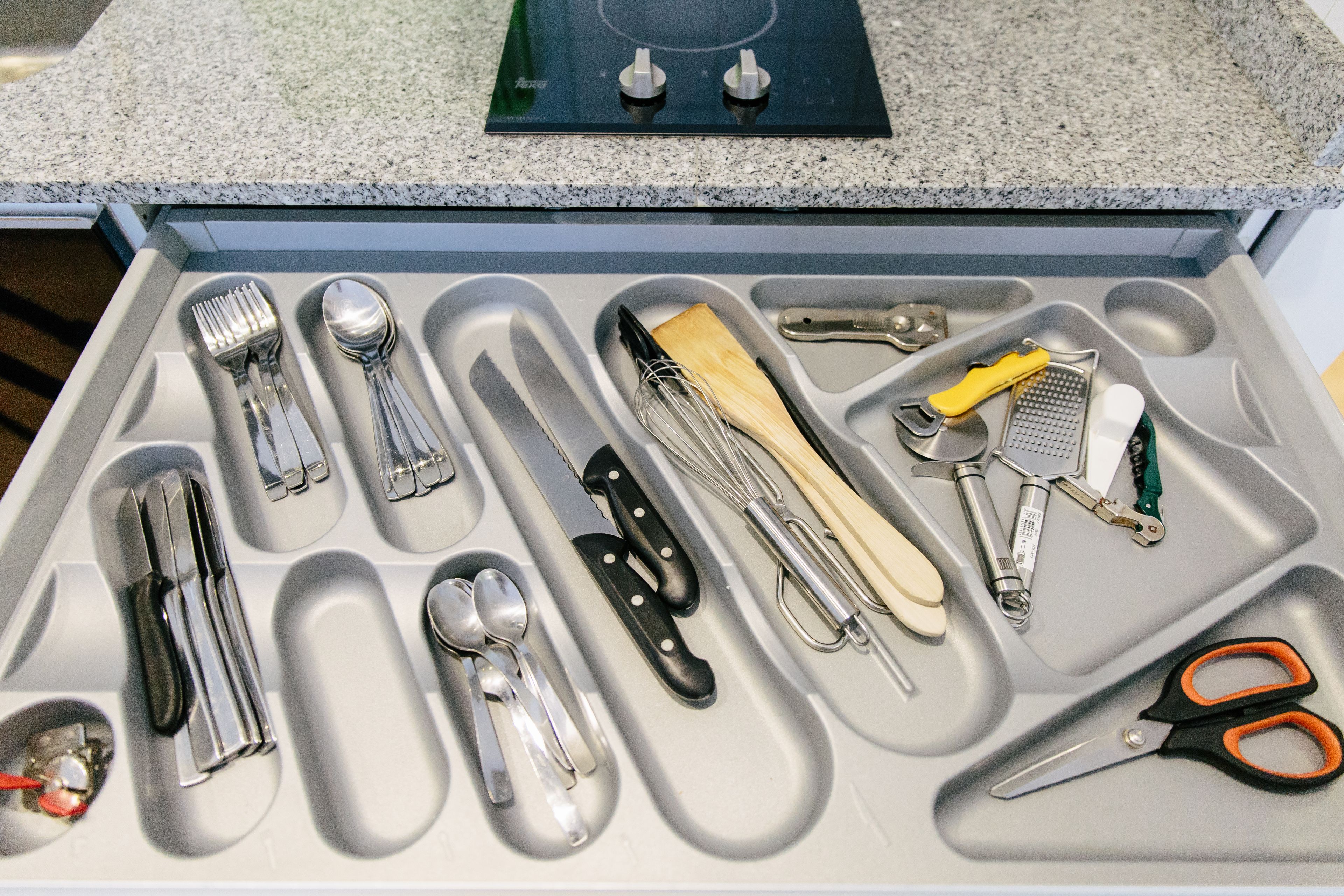 A drawer with various kitchen utensils and tools, including knives, spoons, and a whisk.