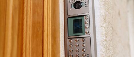 A security keypad with a camera and a digital display, mounted on a textured wall.