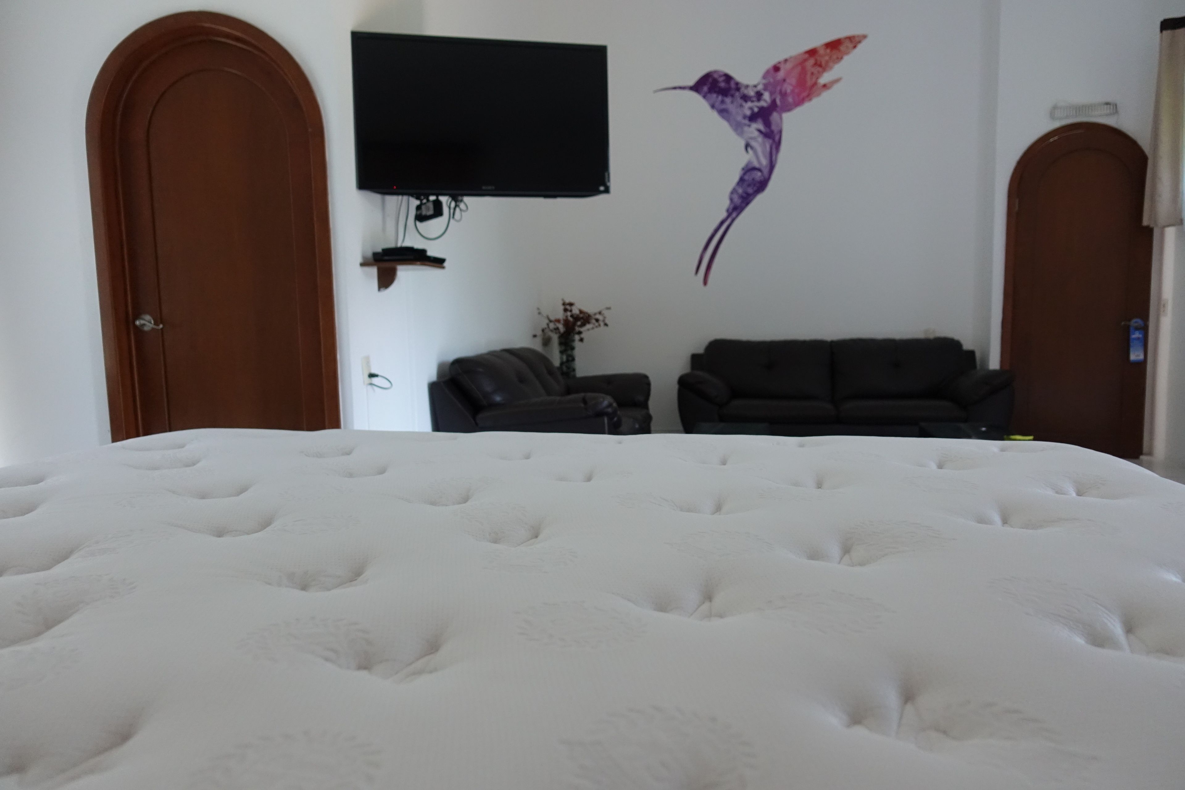 A bedroom with a large bed, a television mounted on the wall, a sofa, and a decorative wall piece.