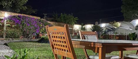 An outdoor dining area with wooden chairs and a table, surrounded by a garden with plants and a stone pathway.