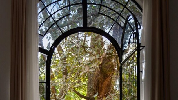 Una habitación con puerta de cristal que da a un jardín, una mesa redonda de cristal y cortinas a ambos lados.