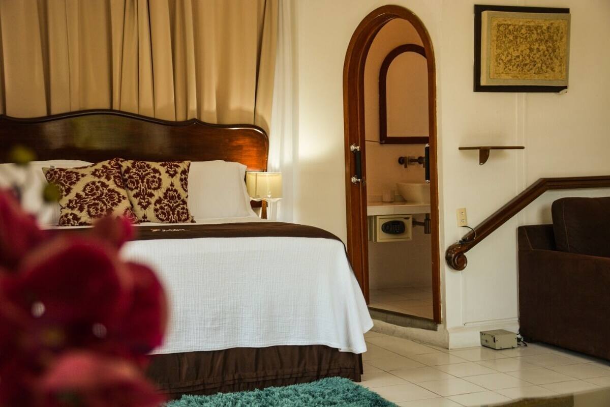 Una habitación de hotel con una cama, una mesita de noche, una lámpara, una puerta de madera y una escalera.