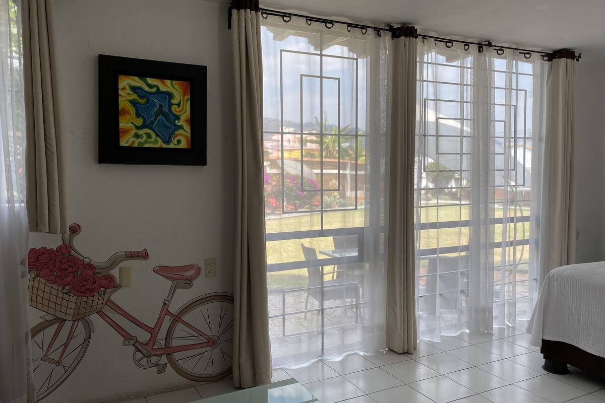 Una habitación de hotel con un ventanal grande, un mural de bicicletas, una cama y una mesa.