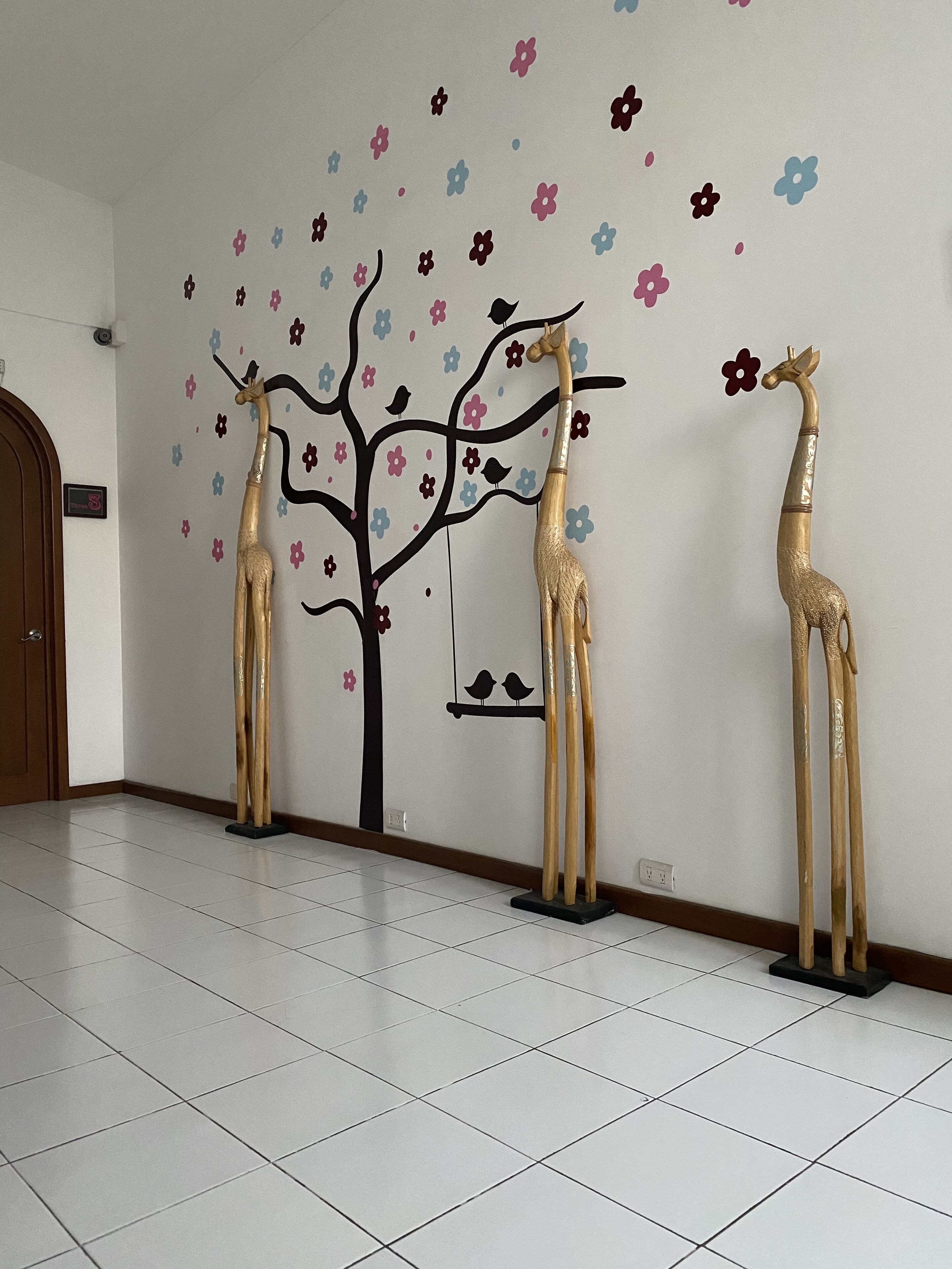 A room with a white tiled floor and a wall decorated with a tree and giraffe decals.