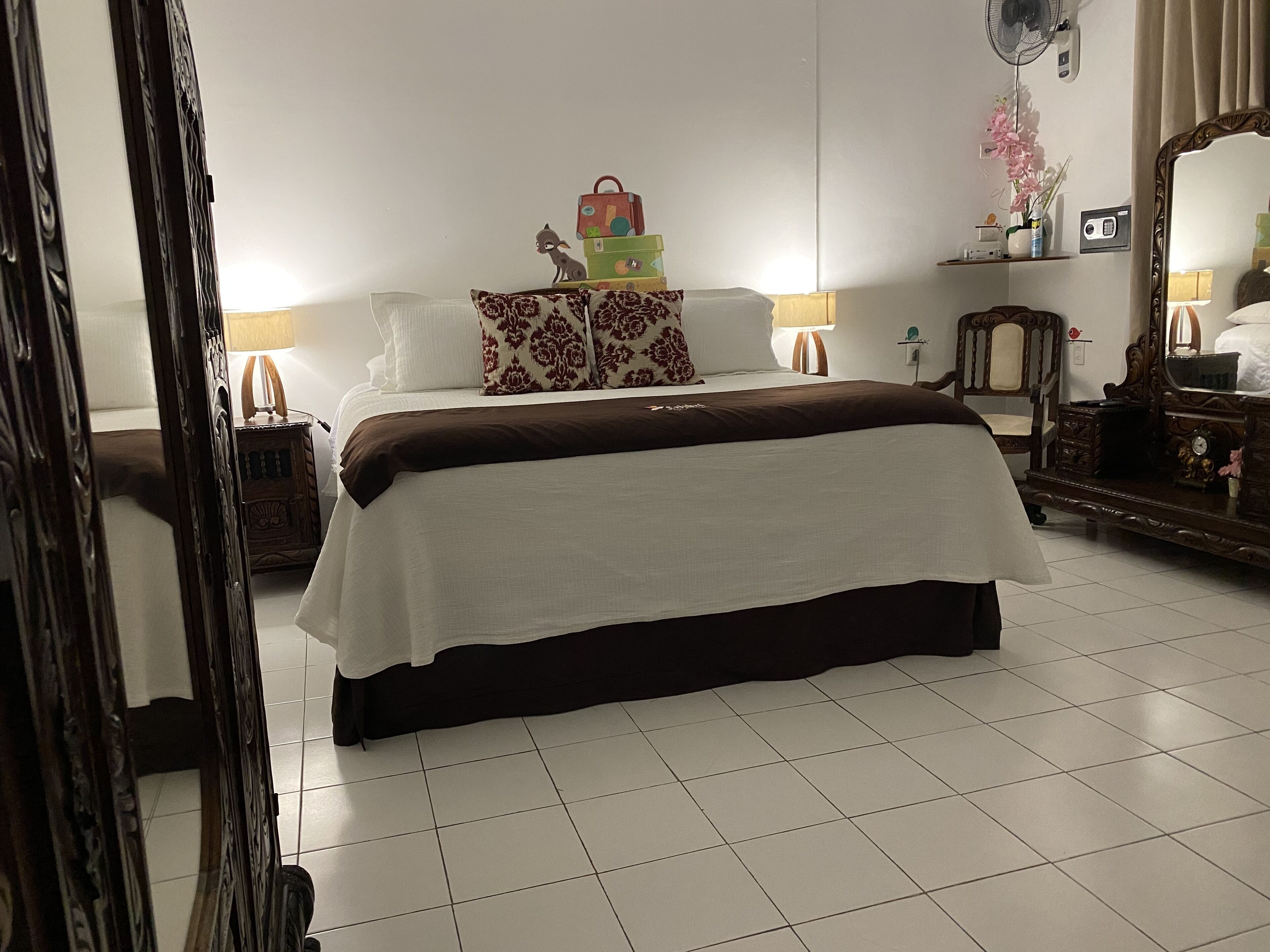A neatly arranged hotel room with a large bed, a wooden nightstand, a dresser, a mirror, and a small table with a lamp.
