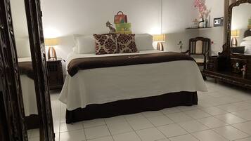 Una habitación de hotel ordenada con una cama grande, una mesita de noche de madera, un aparador, un espejo y una pequeña mesa con una lámpara.