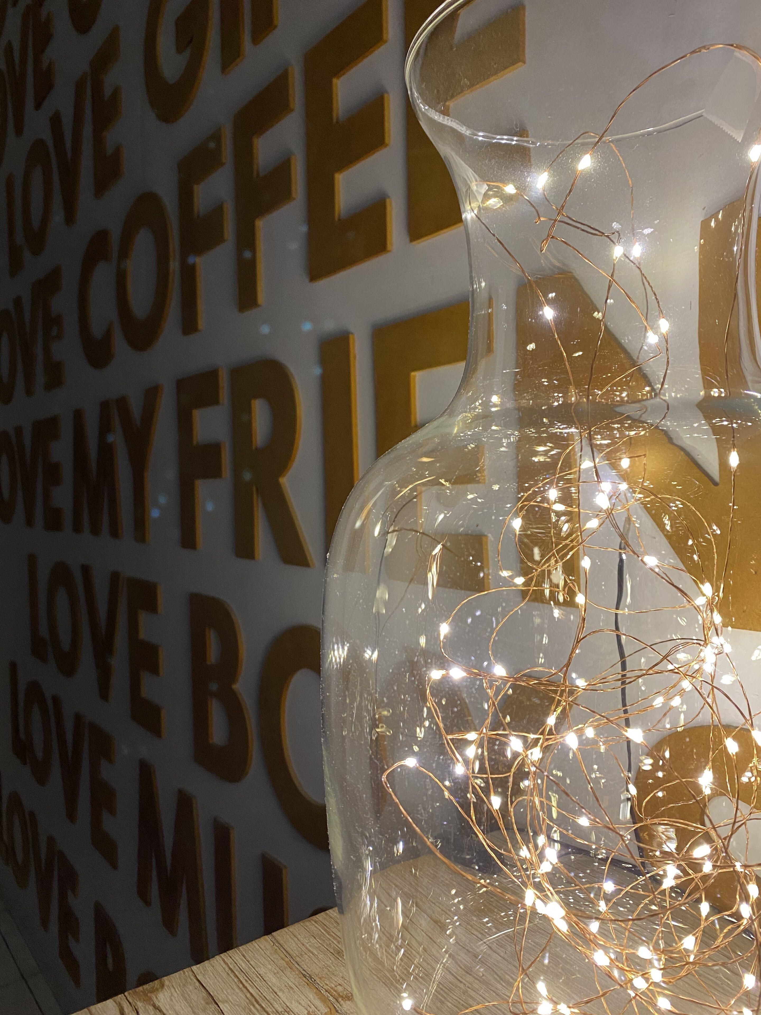 Un florero de vidrio transparente con un diseño texturizado, lleno de luces decorativas, sobre una superficie de madera.