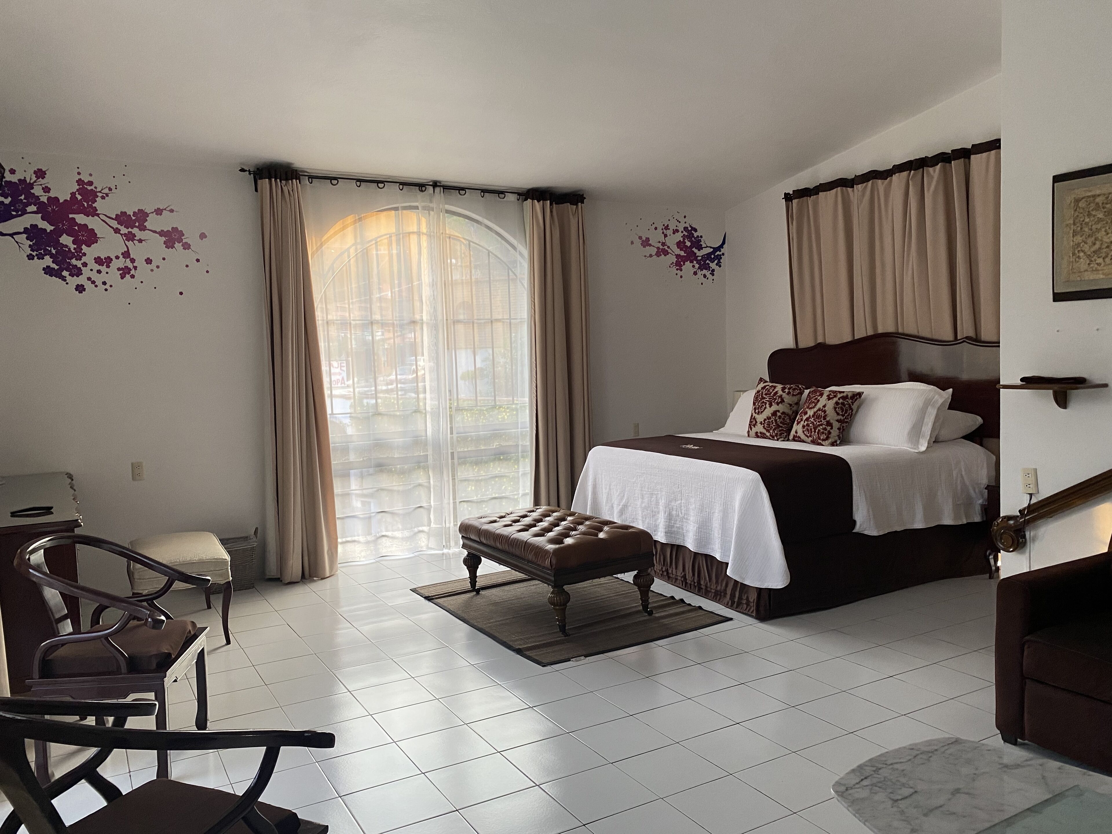 A bedroom with a bed, a chair, a desk, and a large window with curtains.