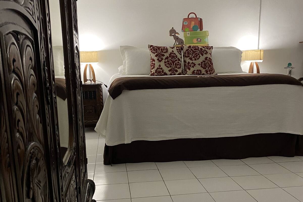 Un dormitorio con una cama grande, un armario de madera y una mesita de noche con una lámpara.