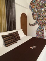 A bed with a striped pillow, a dark brown bedspread, and a colorful elephant mural on the wall.