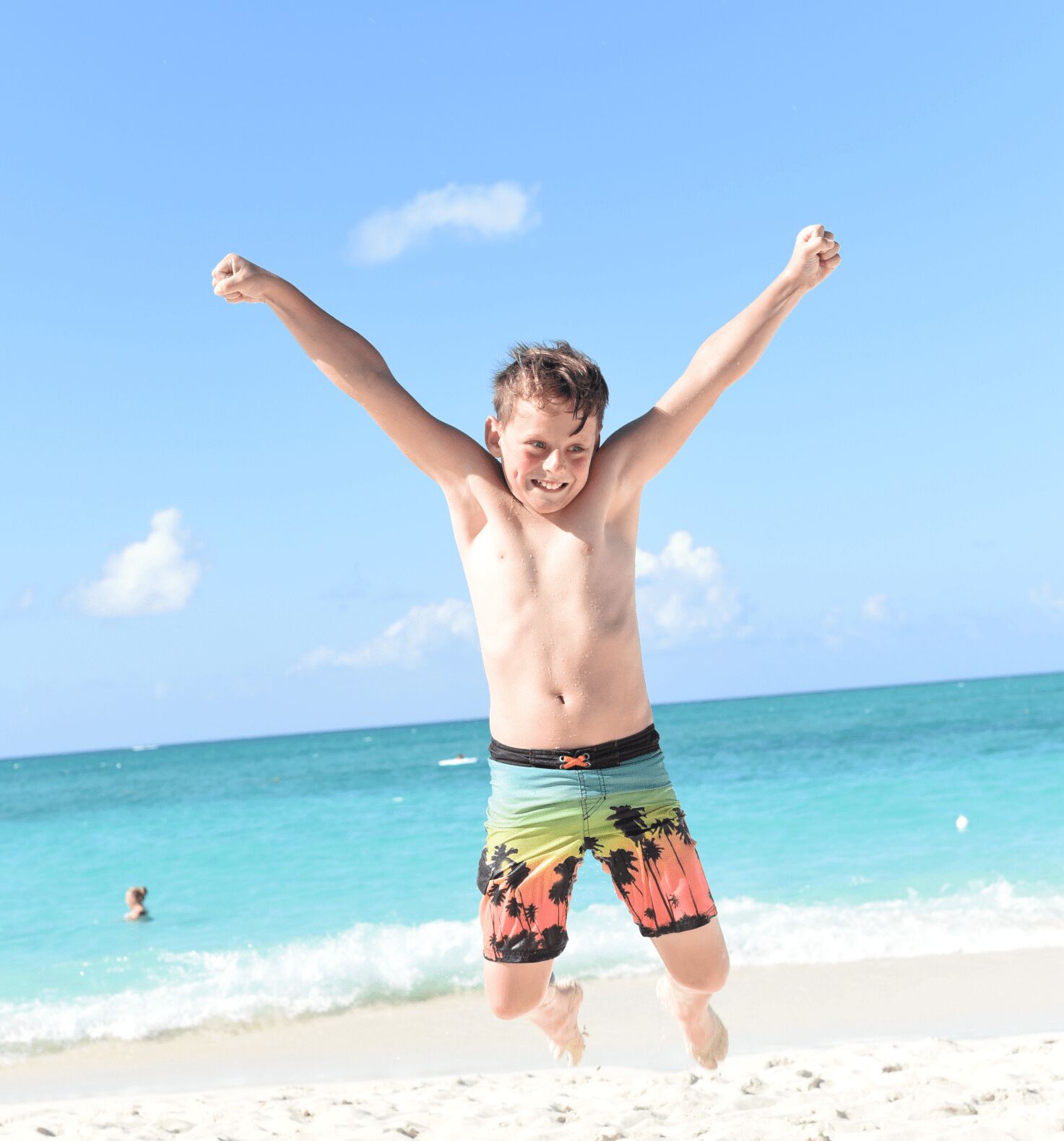 A person jumping on a beach with clear skies and ocean in the background.