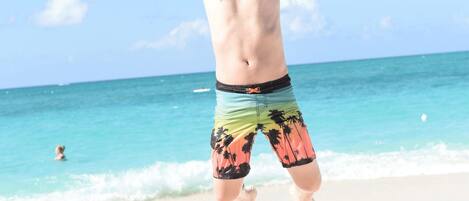 A person jumping on a beach with clear skies and ocean in the background.