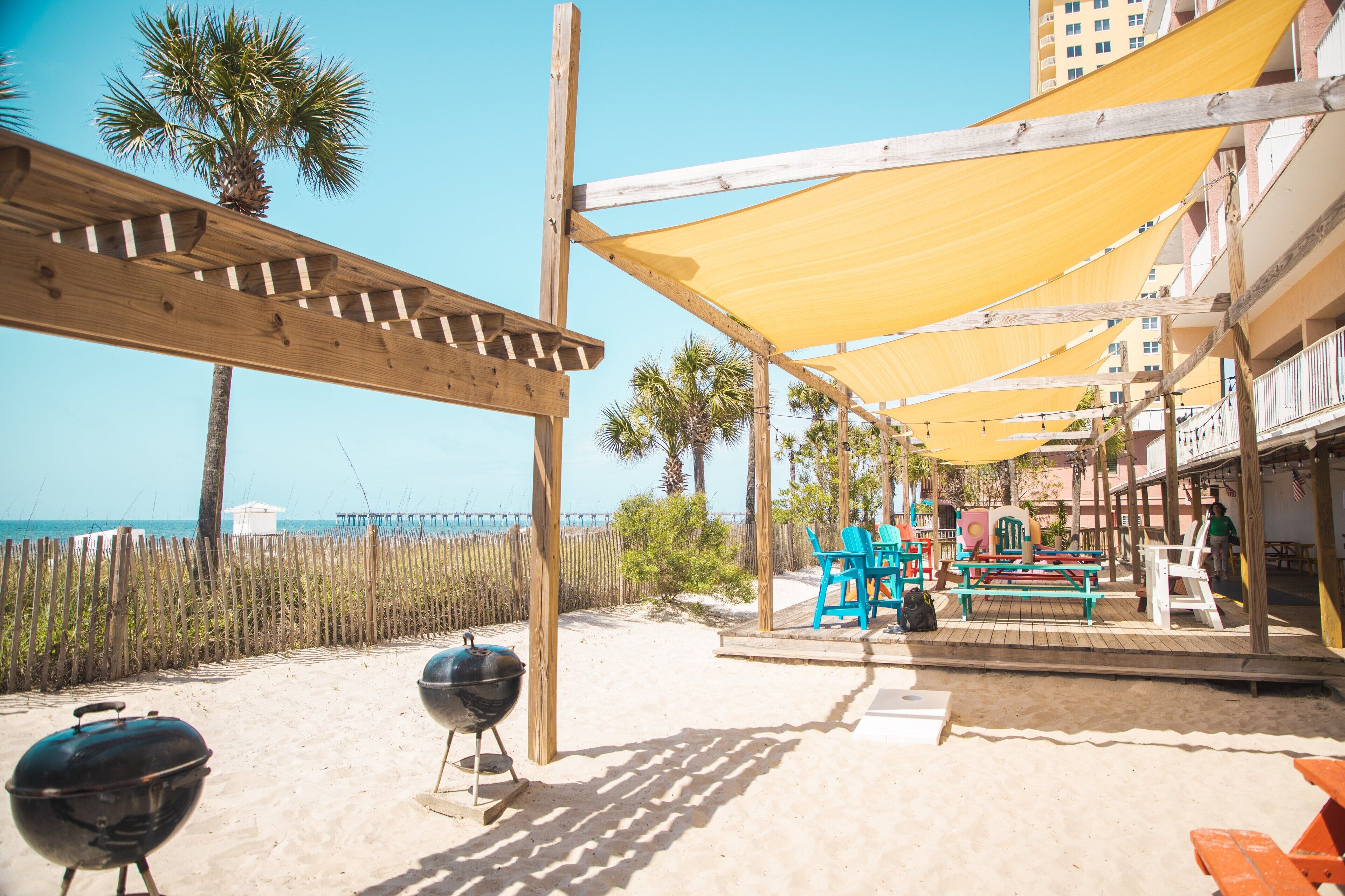 Un patio frente a la playa con pérgolas de madera, asientos al aire libre y vista al océano.