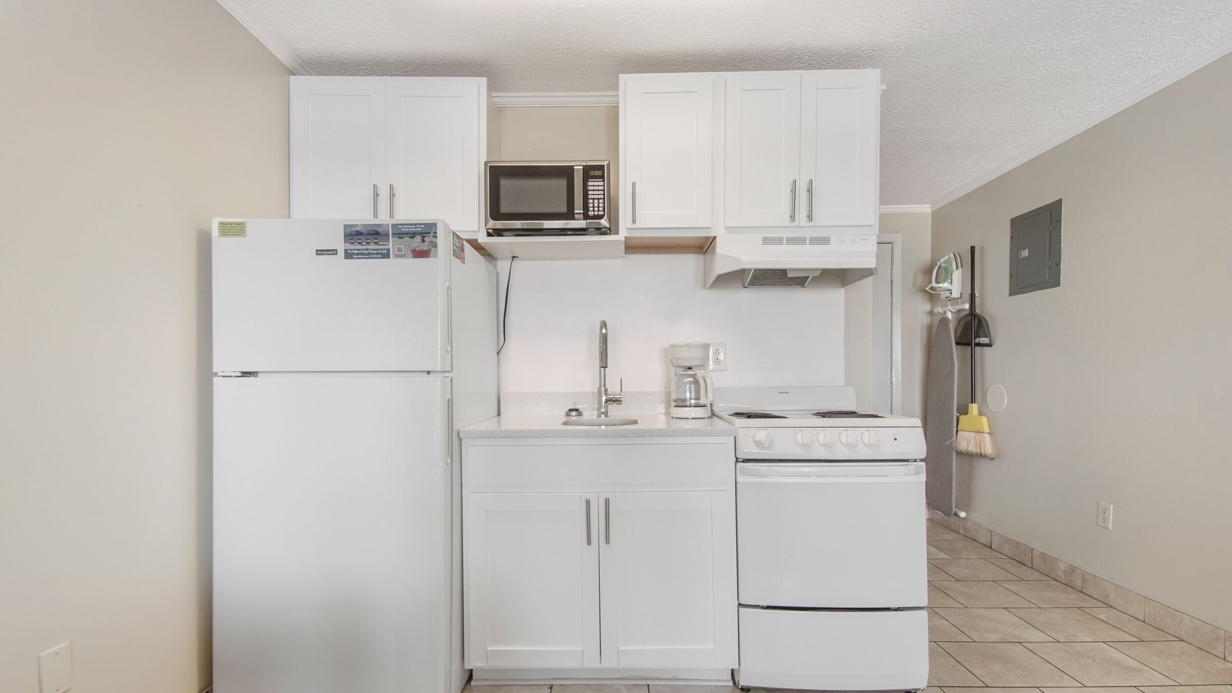 Una cocina compacta con gabinetes blancos, un microondas, una estufa y un refrigerador.