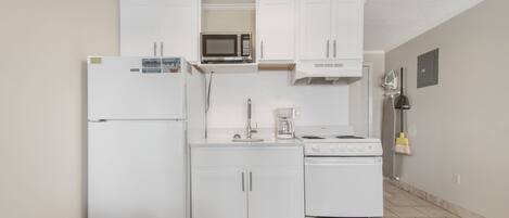 Una cocina compacta con gabinetes blancos, un microondas, una estufa y un refrigerador.