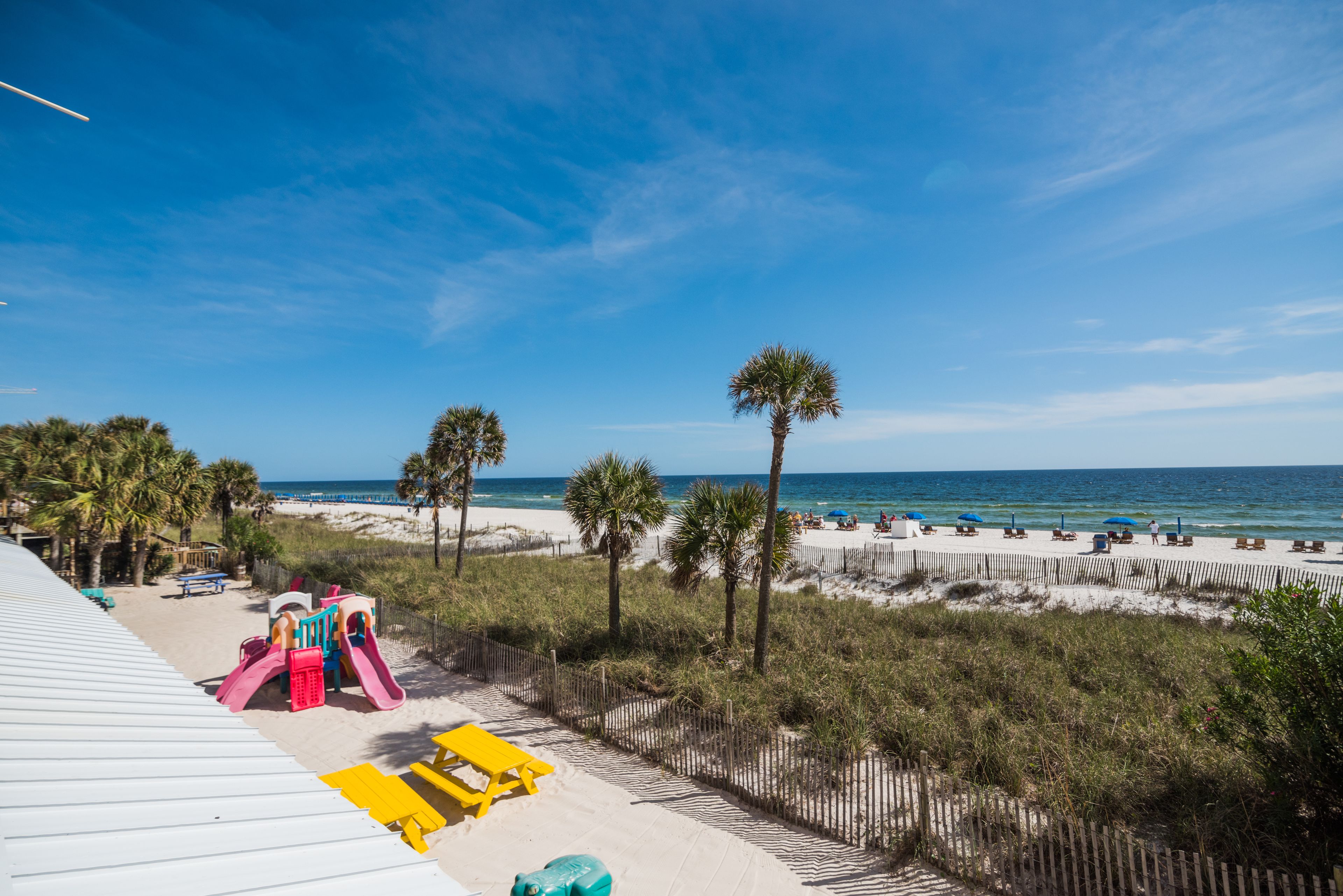 Blick auf einen Strand mit Spielplatz, Palmen und Liegestühlen.