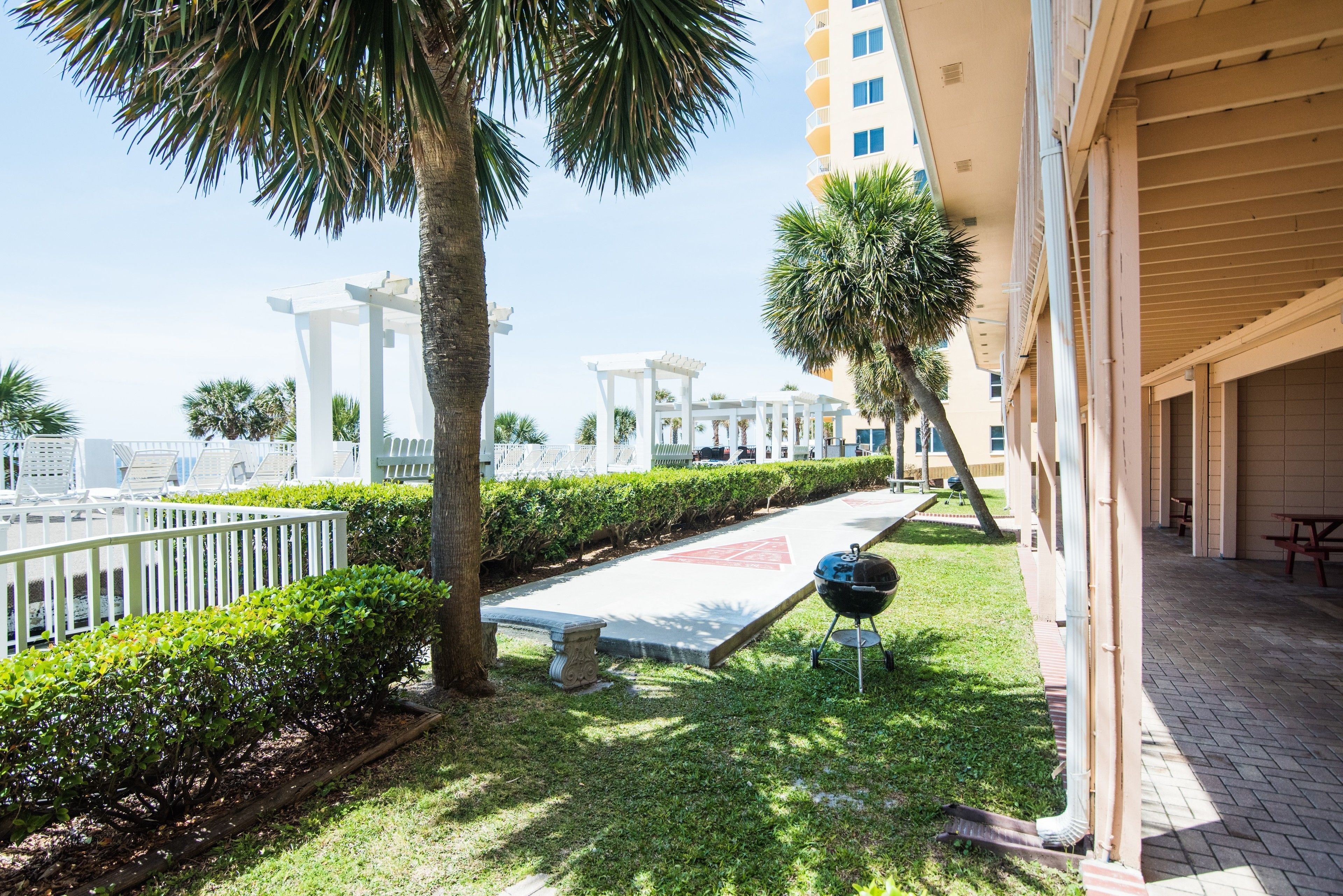 A courtyard with a grill, palm trees, and a white pergola.