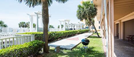 A courtyard with a grill, palm trees, and a white pergola.