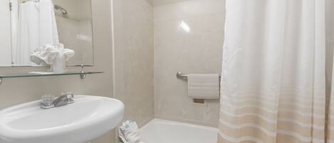 Un baño con un lavabo blanco, estante de vidrio, espejo, toallero y cortina de ducha.