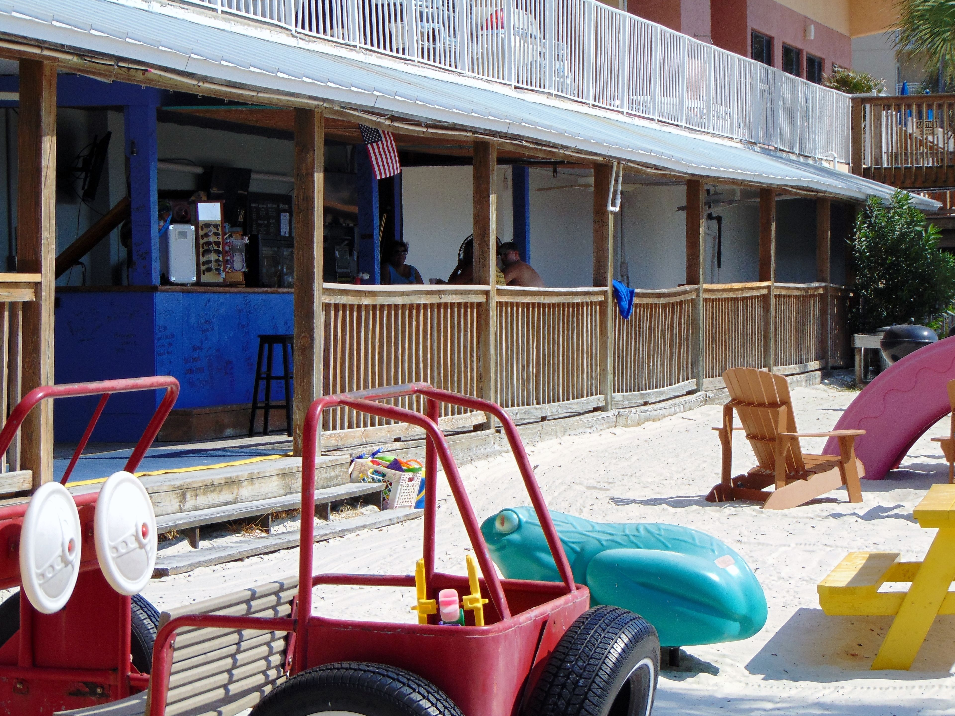 A beachside restaurant with outdoor seating, a red toy car, and inflatable beach chairs.