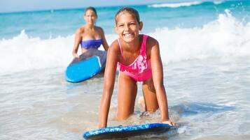 Une personne portant un maillot de bain rose, debout sur une planche de surf bleue, dans l’eau.