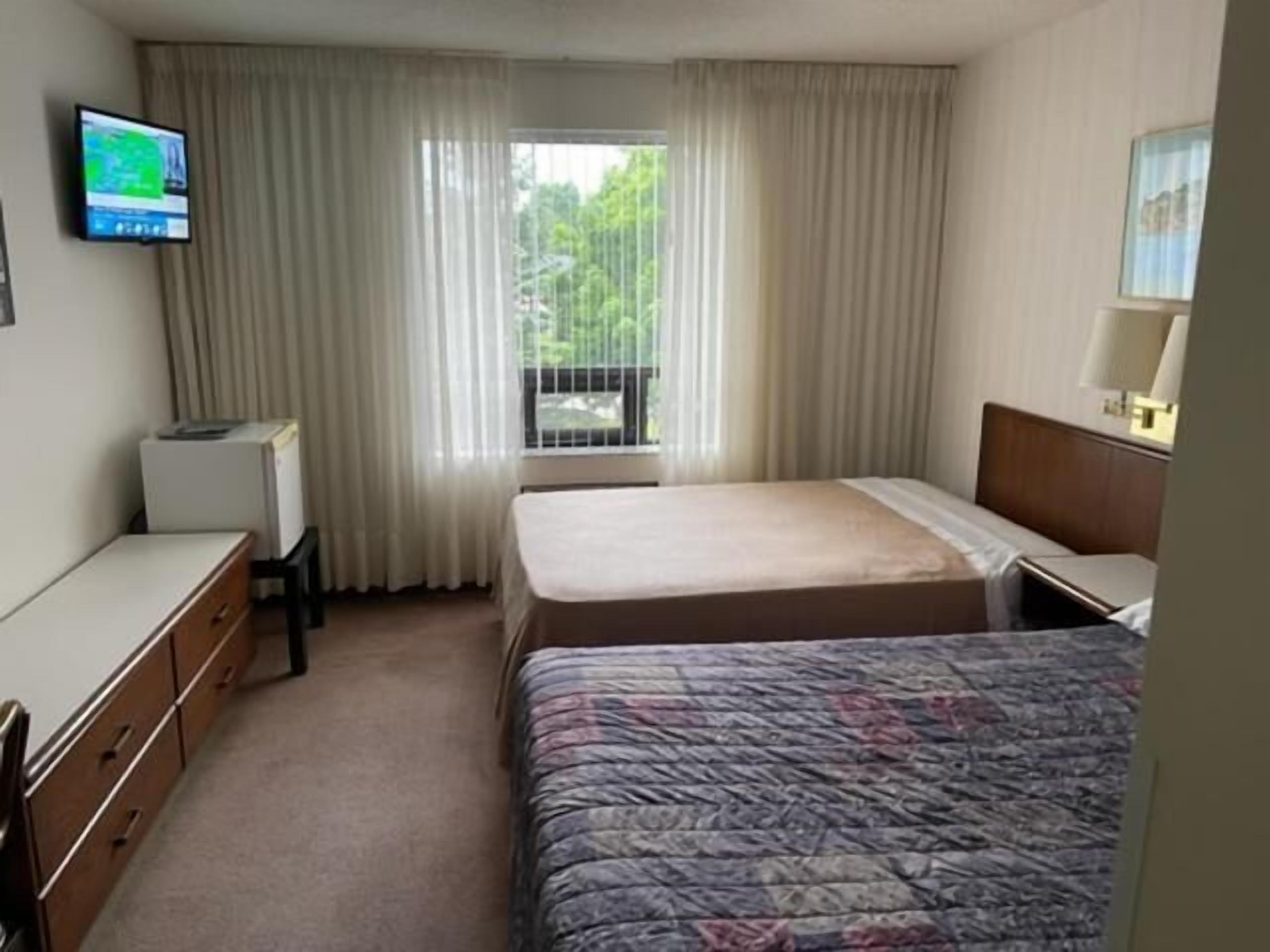A hotel room with a bed, a desk, a chair, a television, and a window with curtains.