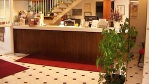 Zona de recepción de un hotel con un mostrador de madera, una escalera y una gran planta en maceta.