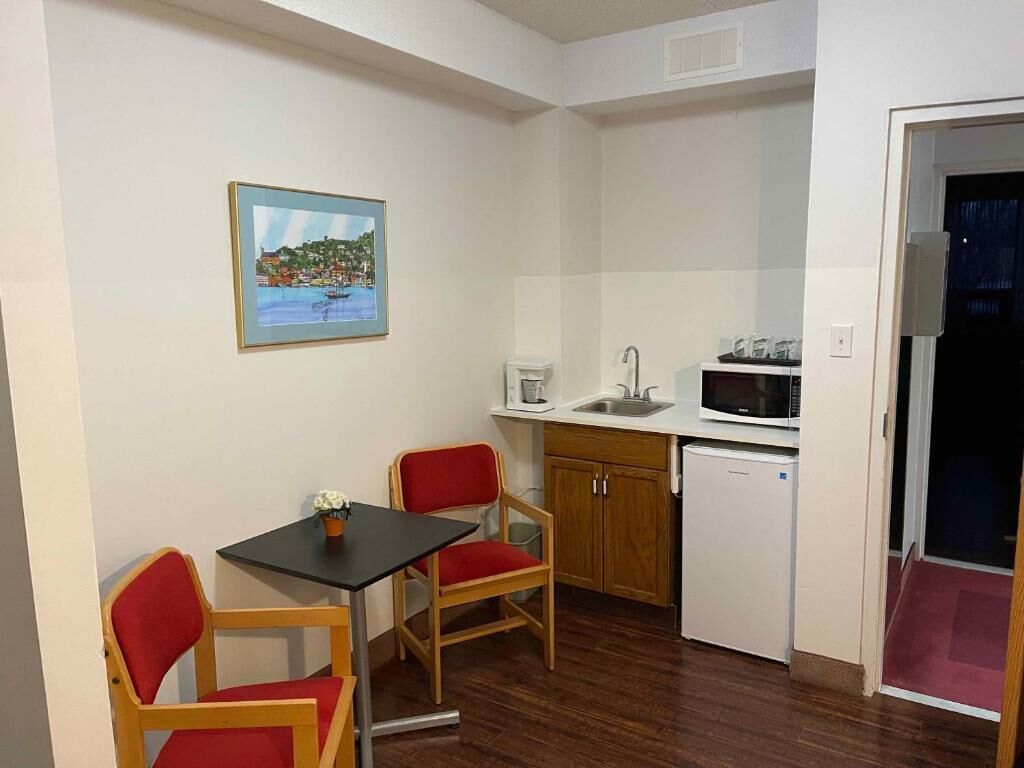A compact kitchen with a microwave, sink, and a small refrigerator. There is a dining area with a table and two chairs. A framed picture hangs on the wall.