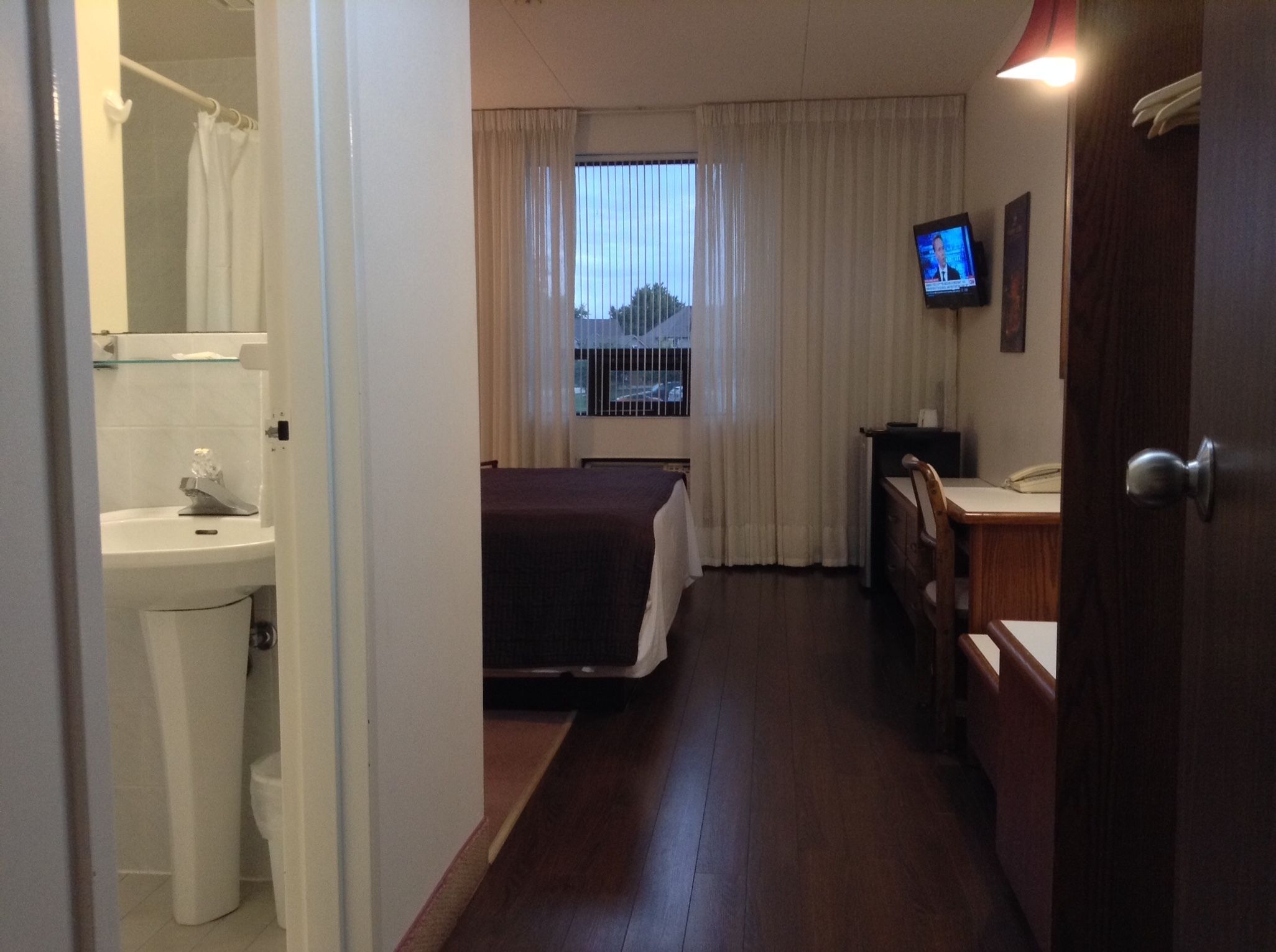 Habitació d'hotel amb llit, escriptori, televisió, bany amb rentapla i vàter, i finestra amb cortines.