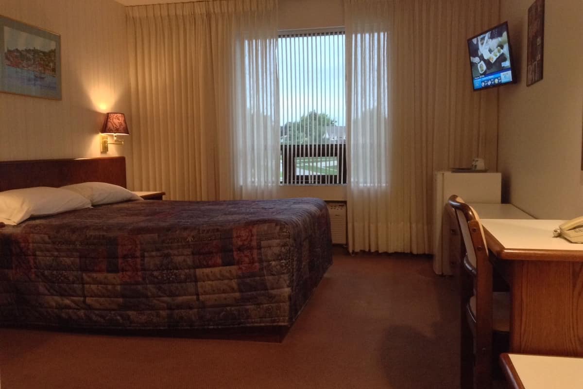 A hotel room with a bed, a desk, a chair, a television, and a window with curtains.