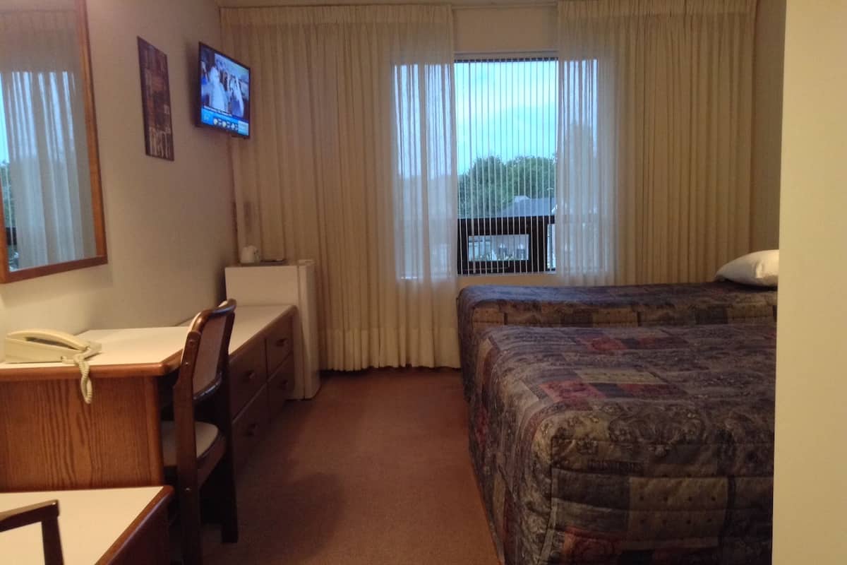 A hotel room with a desk, chair, two beds, a television, and a window with curtains.