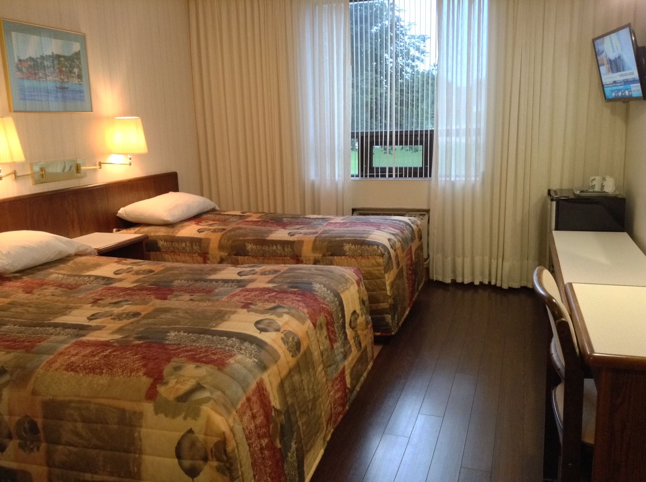 A hotel room with two beds, a desk, a chair, a TV, and a window with curtains.