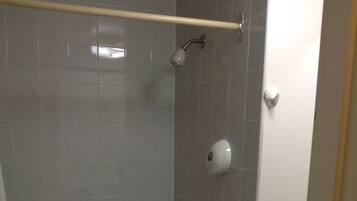 A bathroom with a bathtub, a showerhead, a towel rack, and a hand soap dispenser.