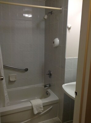 A bathroom with a bathtub, a showerhead, a towel rack, and a hand soap dispenser.