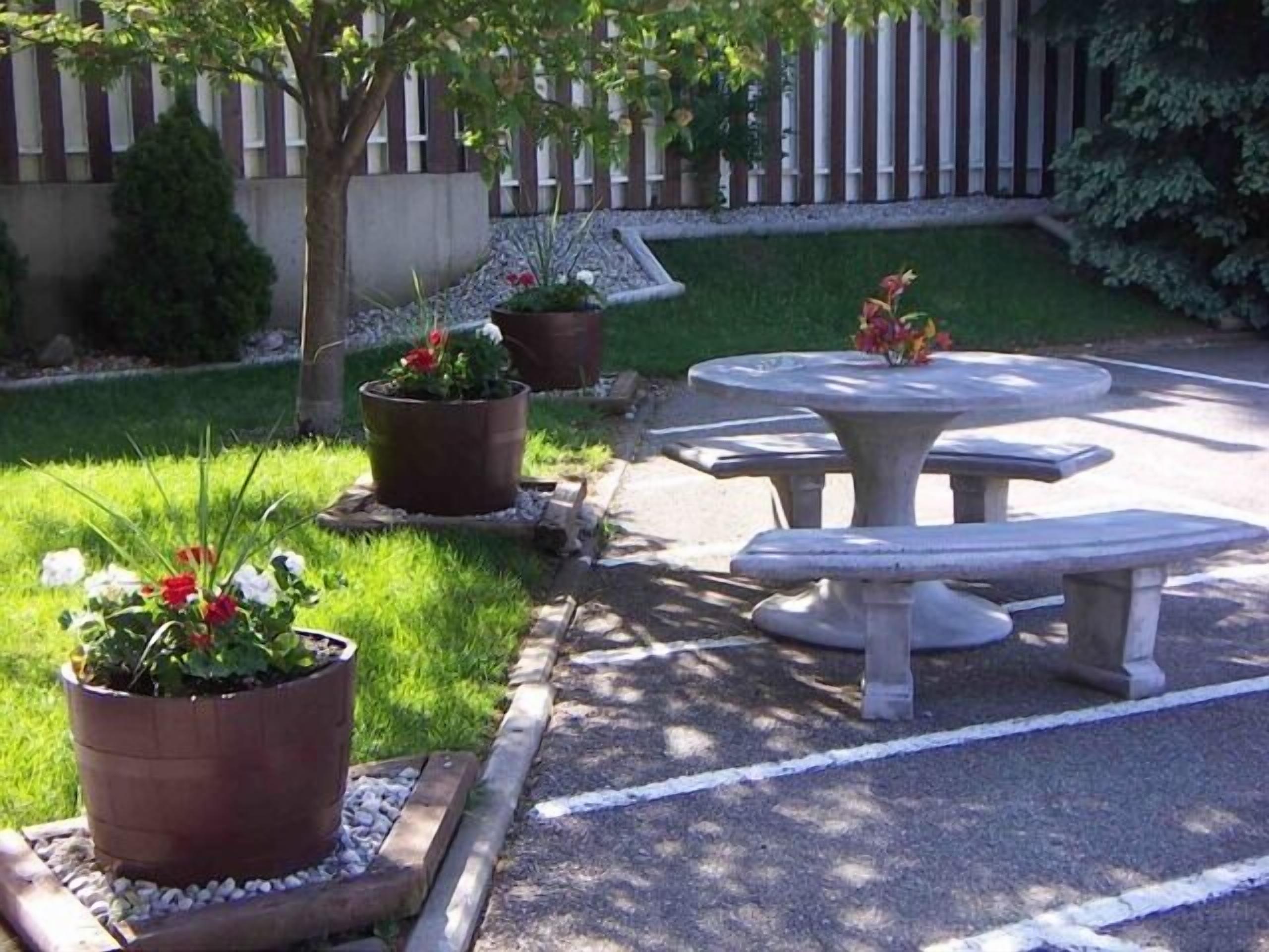Ein Garten mit einem Steintisch, Bänken, Blumentöpfen und einem Holzzaun.