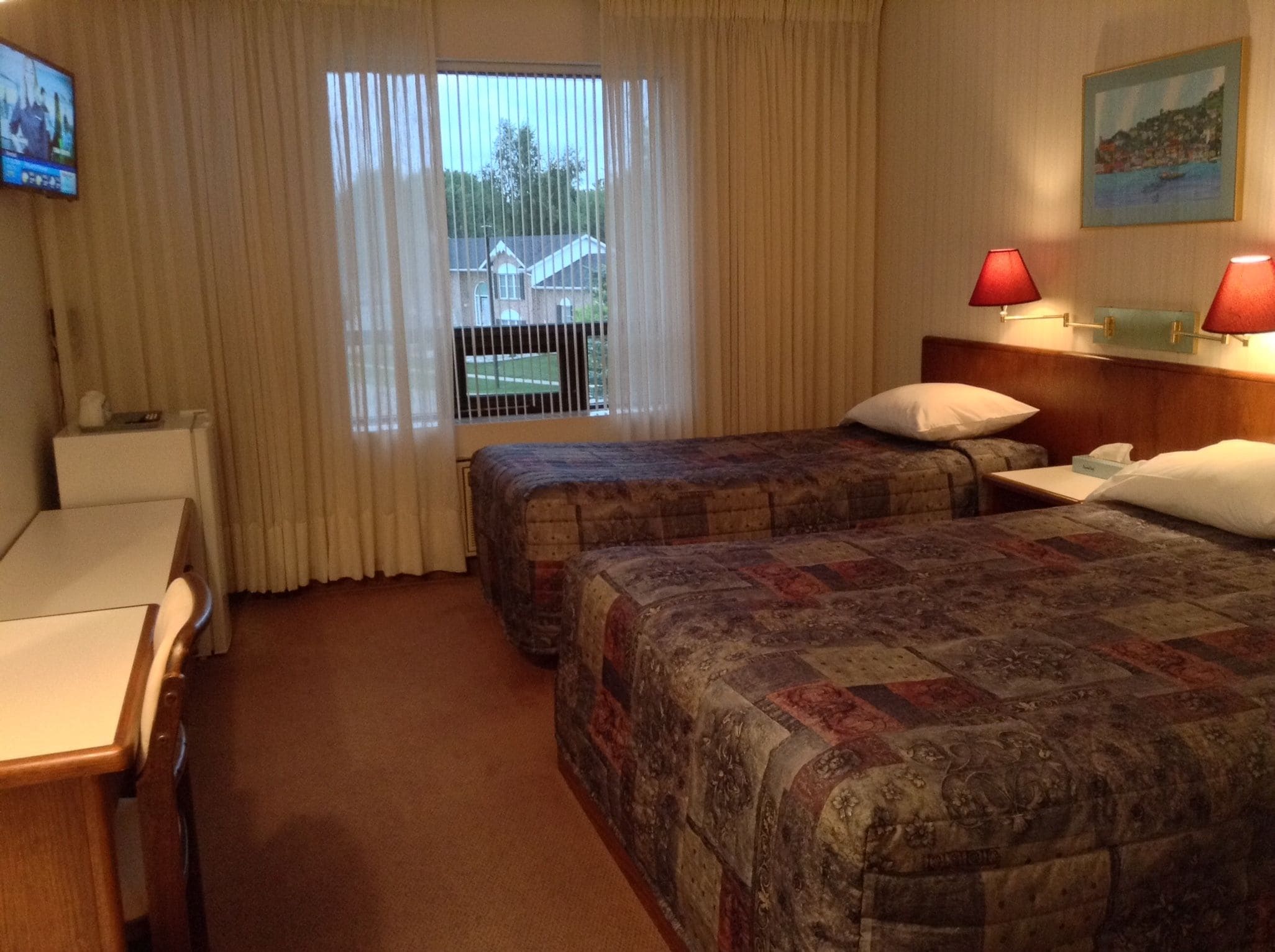 A hotel room with two beds, a desk, a chair, a TV, and a window with curtains.