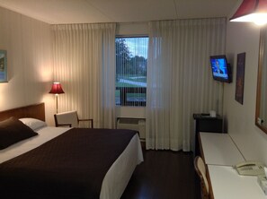 A hotel room with a bed, a desk, a chair, a TV, and a window with curtains.
