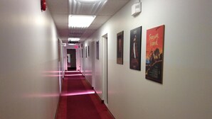 Un pasillo con alfombra roja, paredes blancas y carteles enmarcados a la derecha.