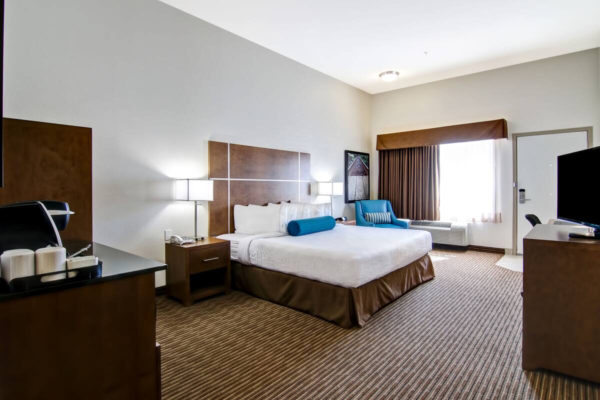 Habitación de hotel con una cama grande, un escritorio con ordenador, una silla, televisor y ventana con cortinas.