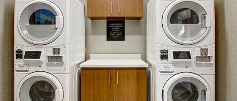 A laundry area with two front-loading washing machines, a wooden cabinet, and a sign indicating no oil use.